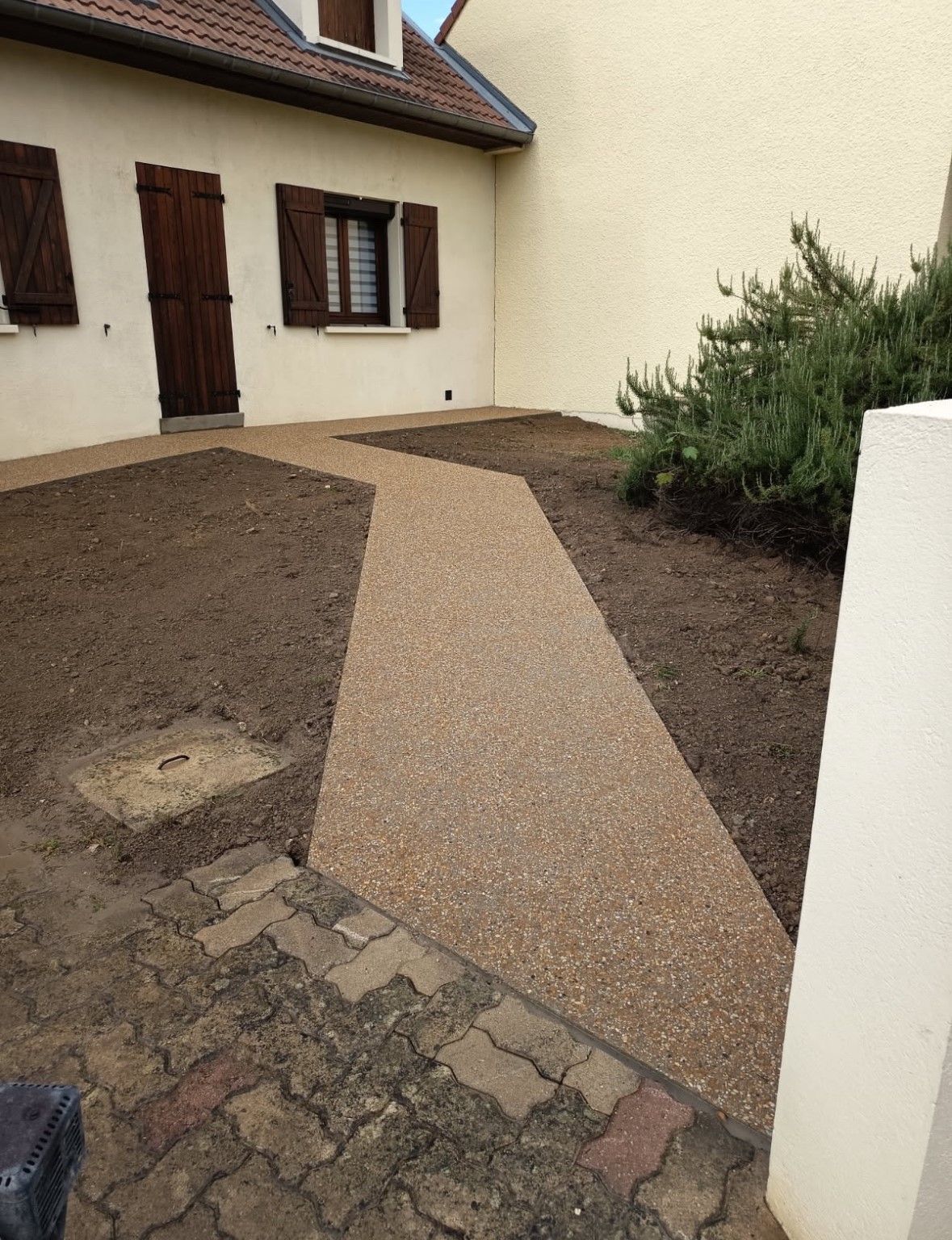 Chemin de pierres tachetées traversant la cour, menant à l'entrée de la maison. Couleurs marron et beige.