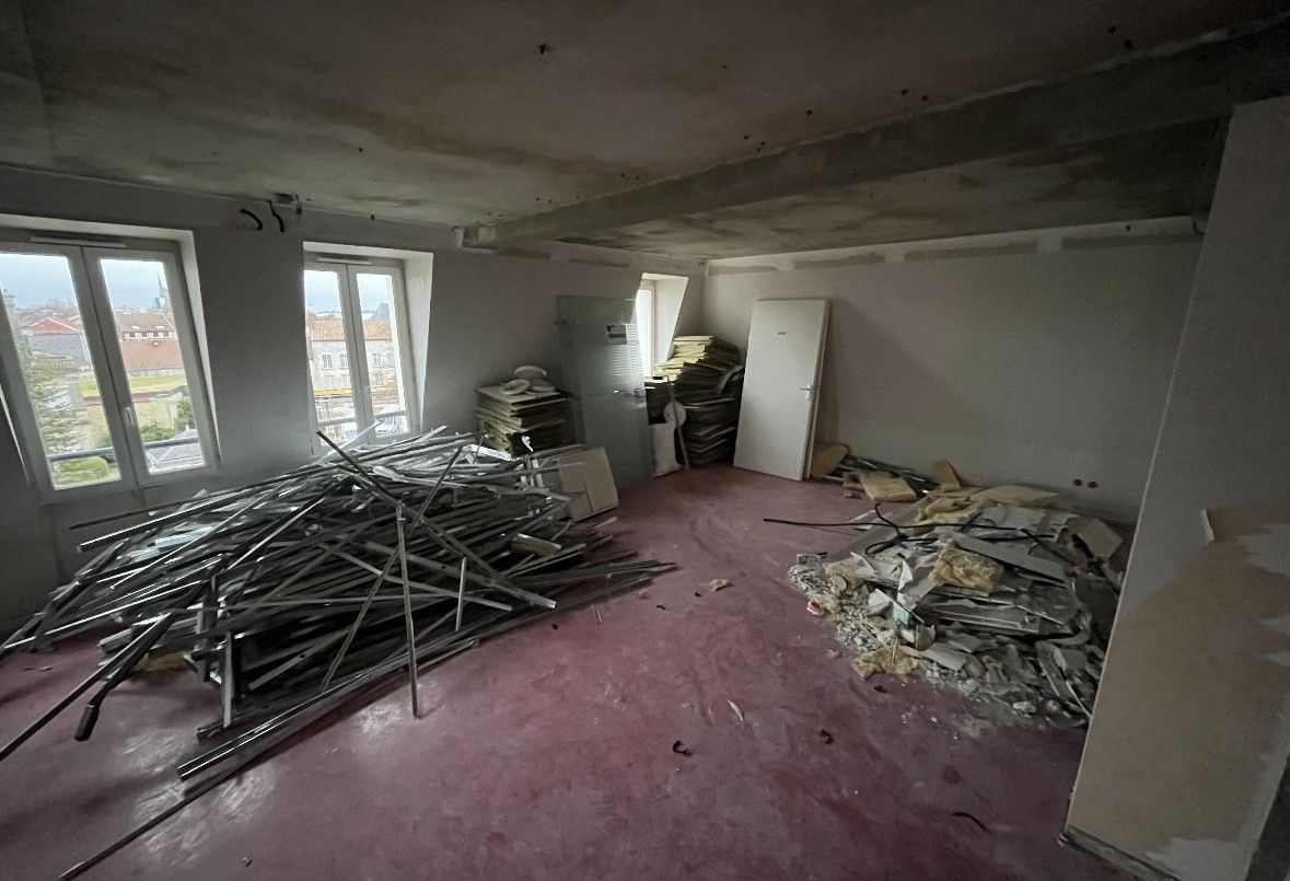 Chambre en rénovation avec débris, barreaux métalliques, sol rose et fenêtres.