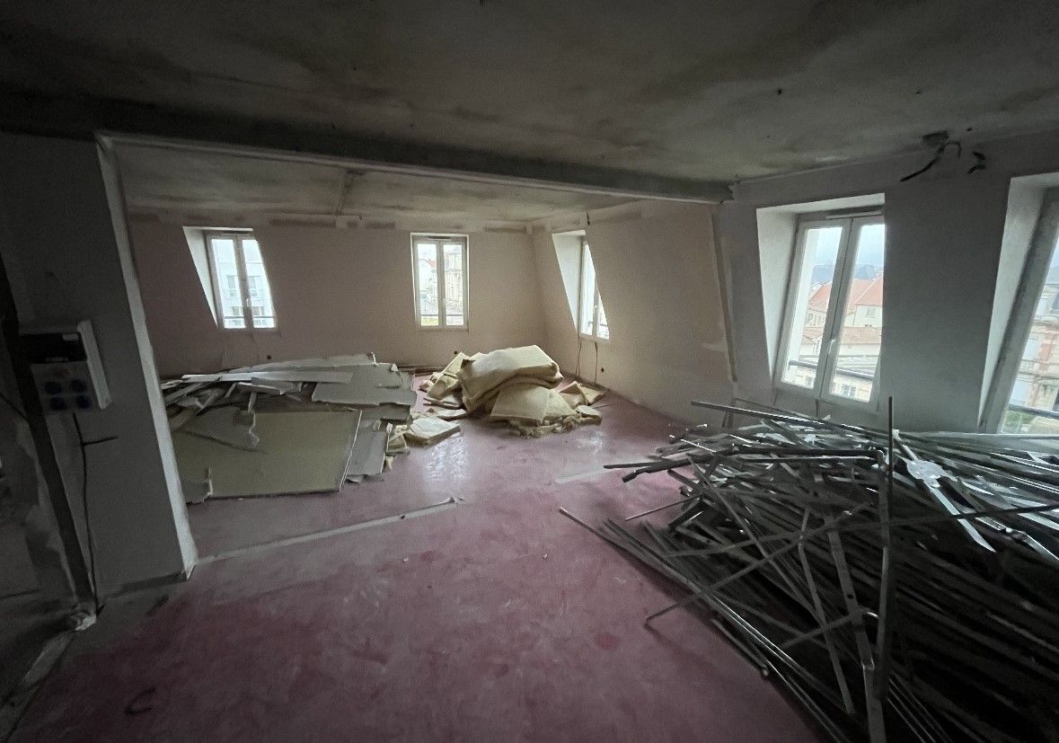 Chambre en cours de rénovation; sol rose, débris, fenêtres, tiges métalliques.