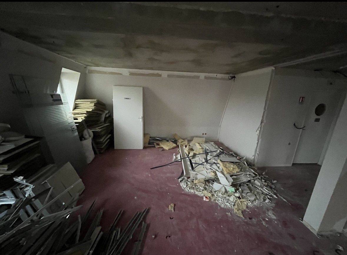 Pièce en désordre avec des débris sur le tapis rouge. Porte et murs blancs, plafond en béton.