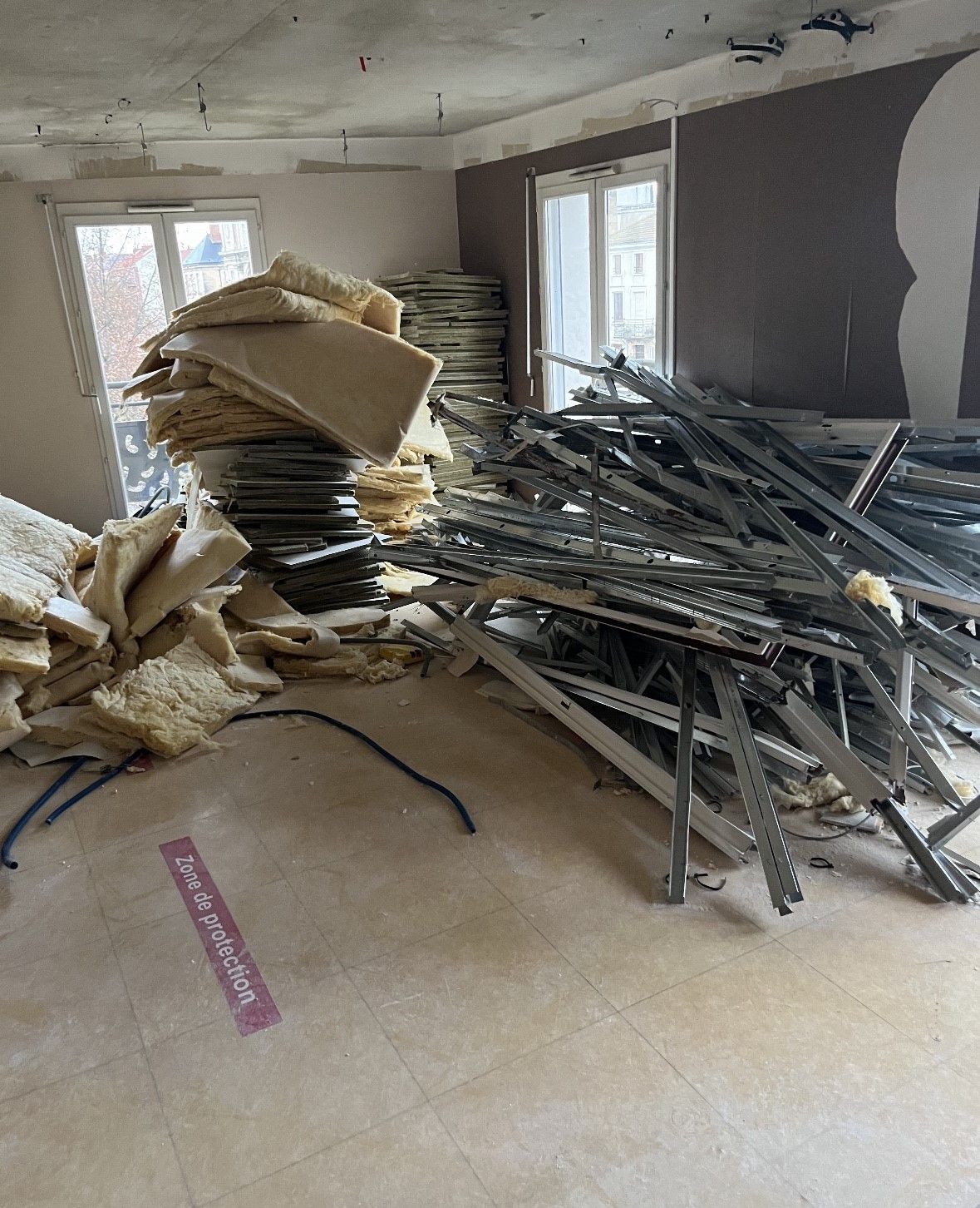 Démolition intérieure, tas de débris dans une pièce avec deux fenêtres et montants muraux exposés.