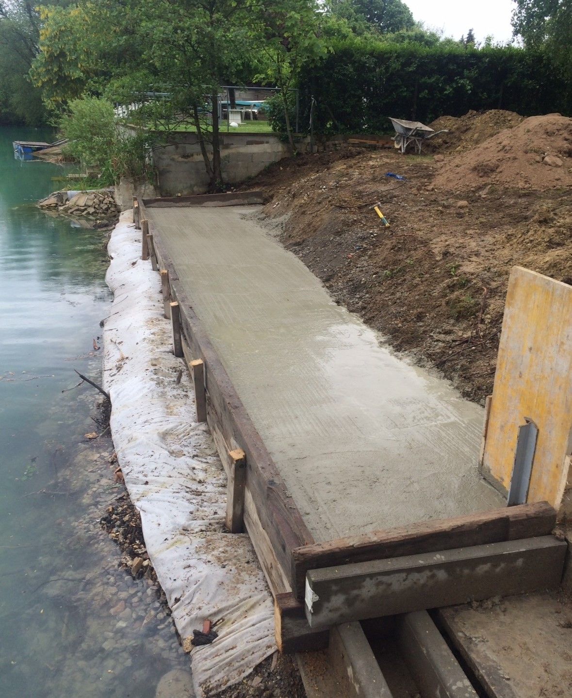 Construction d'un chemin en béton le long d'un cours d'eau turquoise ; coffrage en bois visible.