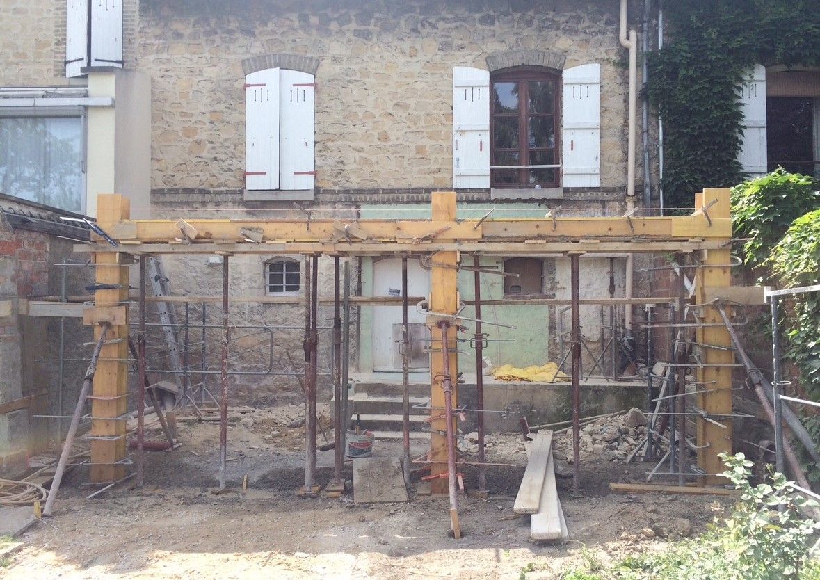 Chantier avec ossature en bois, structure portante contre bâtiment en briques, aménagement extérieur.