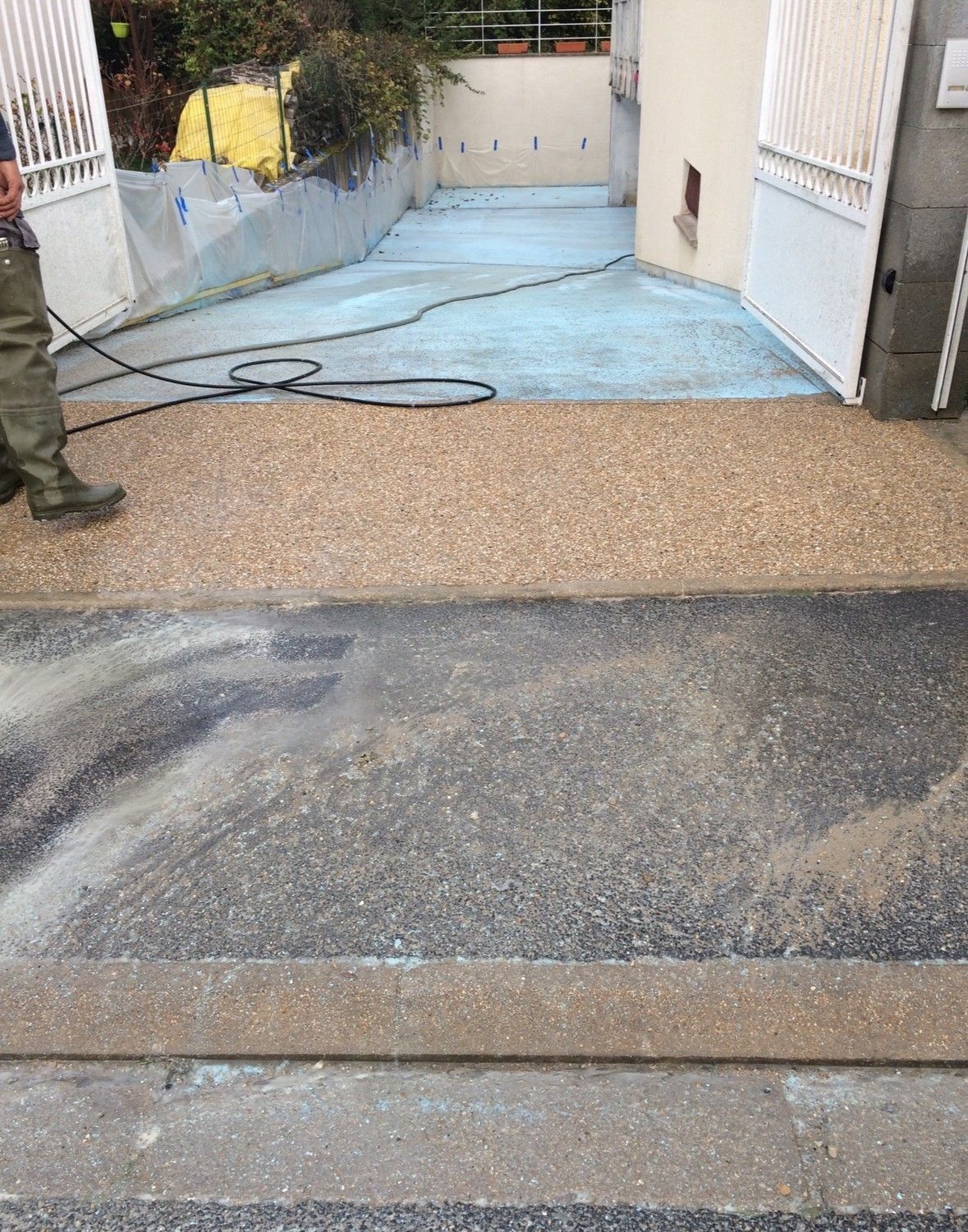 Une personne nettoie une allée à haute pression, montrant la section nettoyée et plus claire et la section sale.