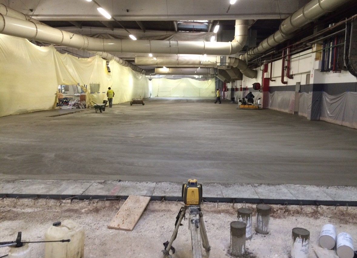 Un sol en béton est coulé dans un espace intérieur, avec des ouvriers et du matériel visibles.