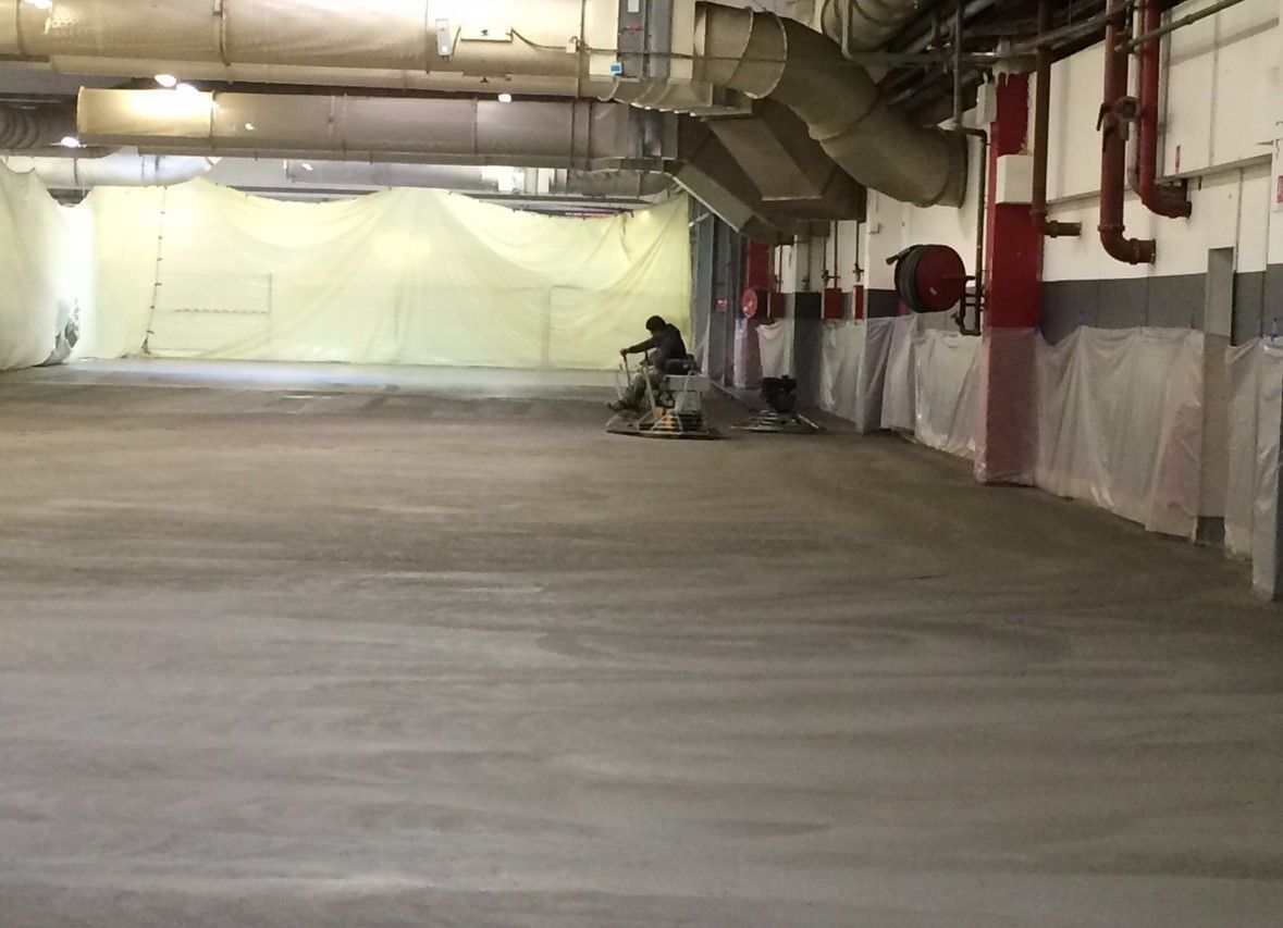 Personne utilisant une ponceuse à sol dans un grand espace industriel vide.