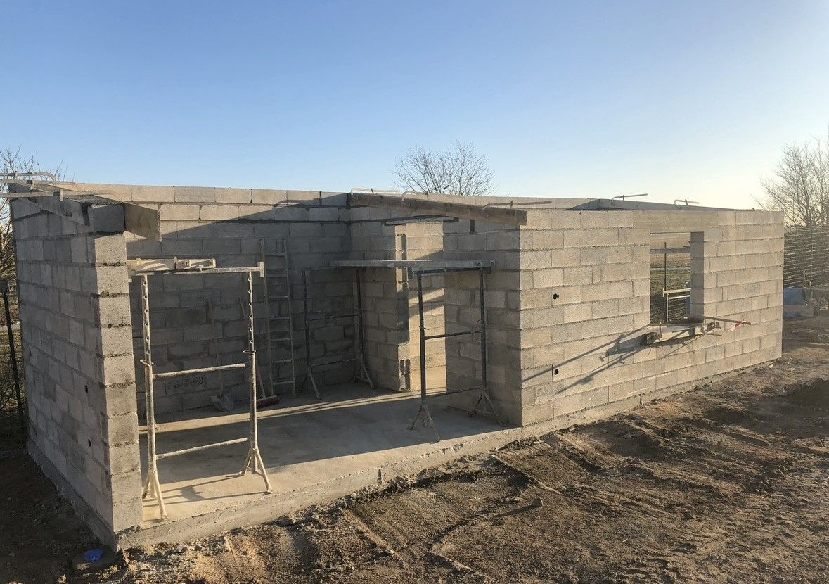 Un bâtiment en blocs de béton en construction avec des ouvertures de fenêtres et de portes, à l'extérieur.
