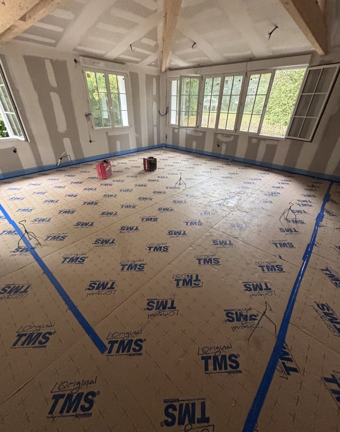 Intérieur de la pièce en construction : cloisons sèches, fenêtres et ruban adhésif bleu sur un plancher en bois.