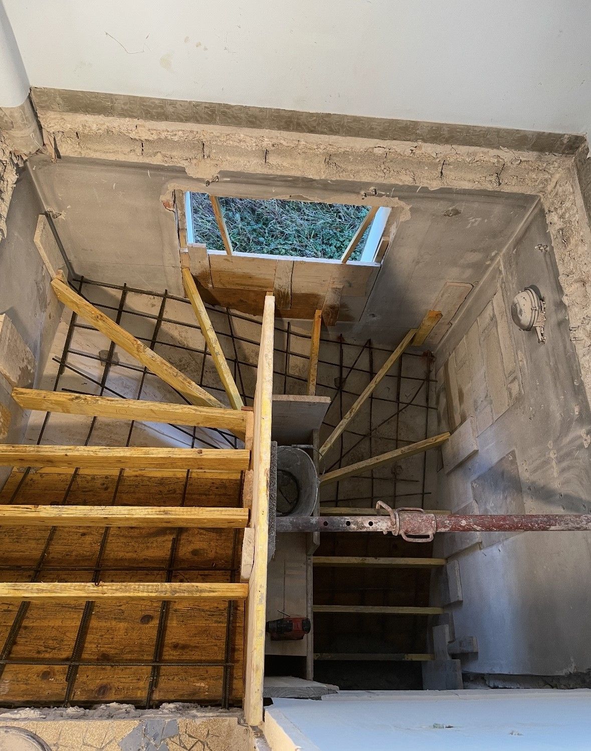 Escalier en construction avec coffrages en bois, barres d'armature et puits de lumière au-dessus.