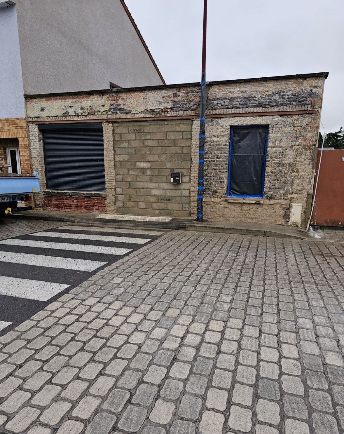 Bâtiment en briques avec devanture fermée, entrée bloquée et rue pavée.