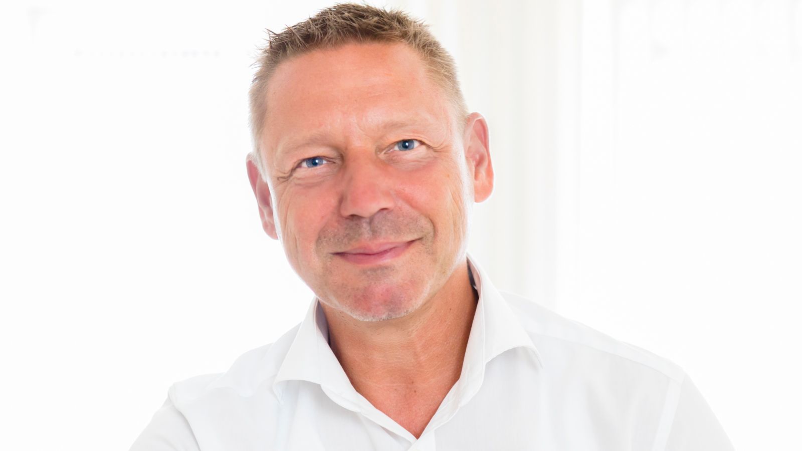 Ein Mann in einem weißen Hemd lächelt und schaut in die Kamera.