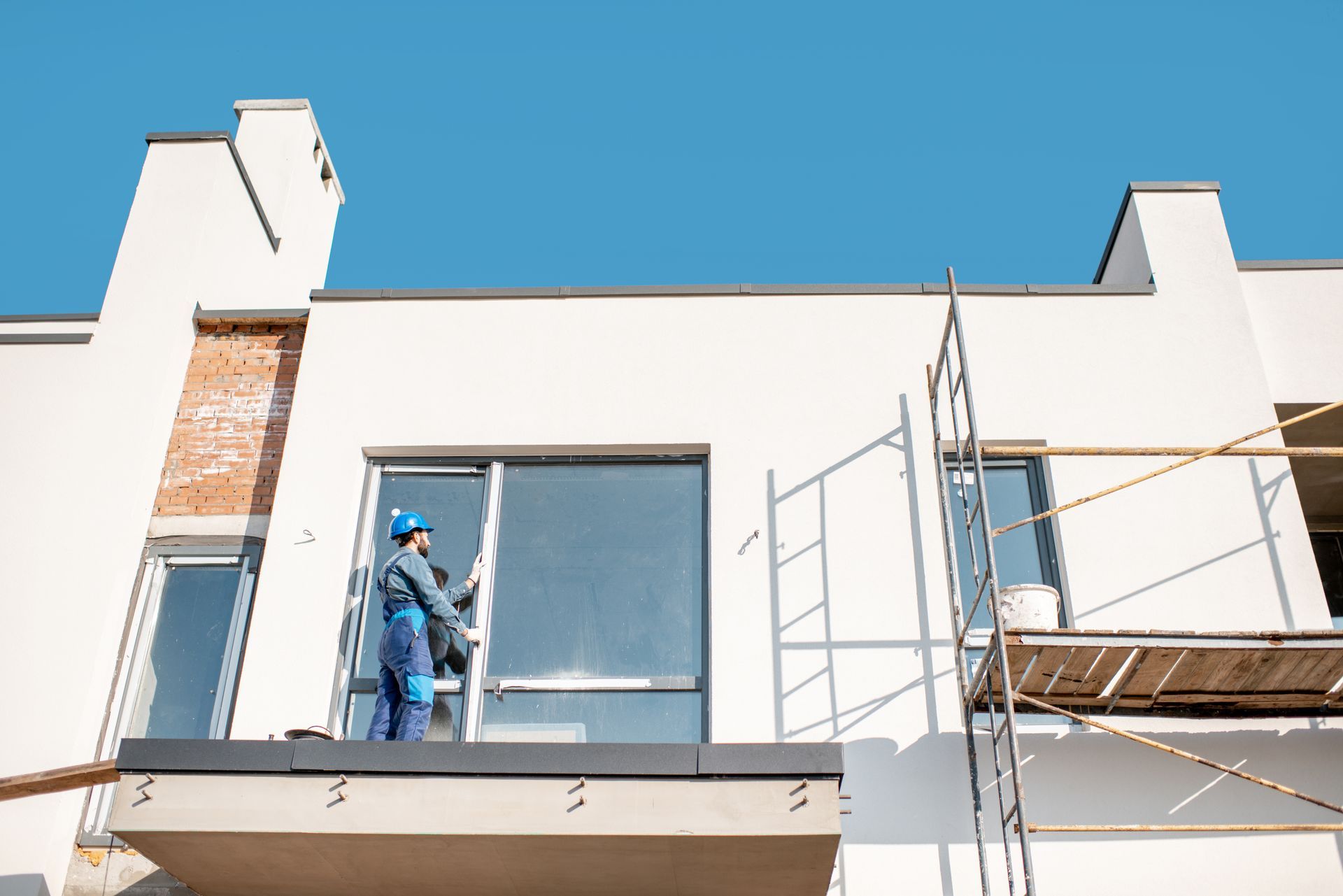Des ouvriers sur des échafaudages peignent la façade blanche d'un bâtiment moderne sous un ciel bleu.