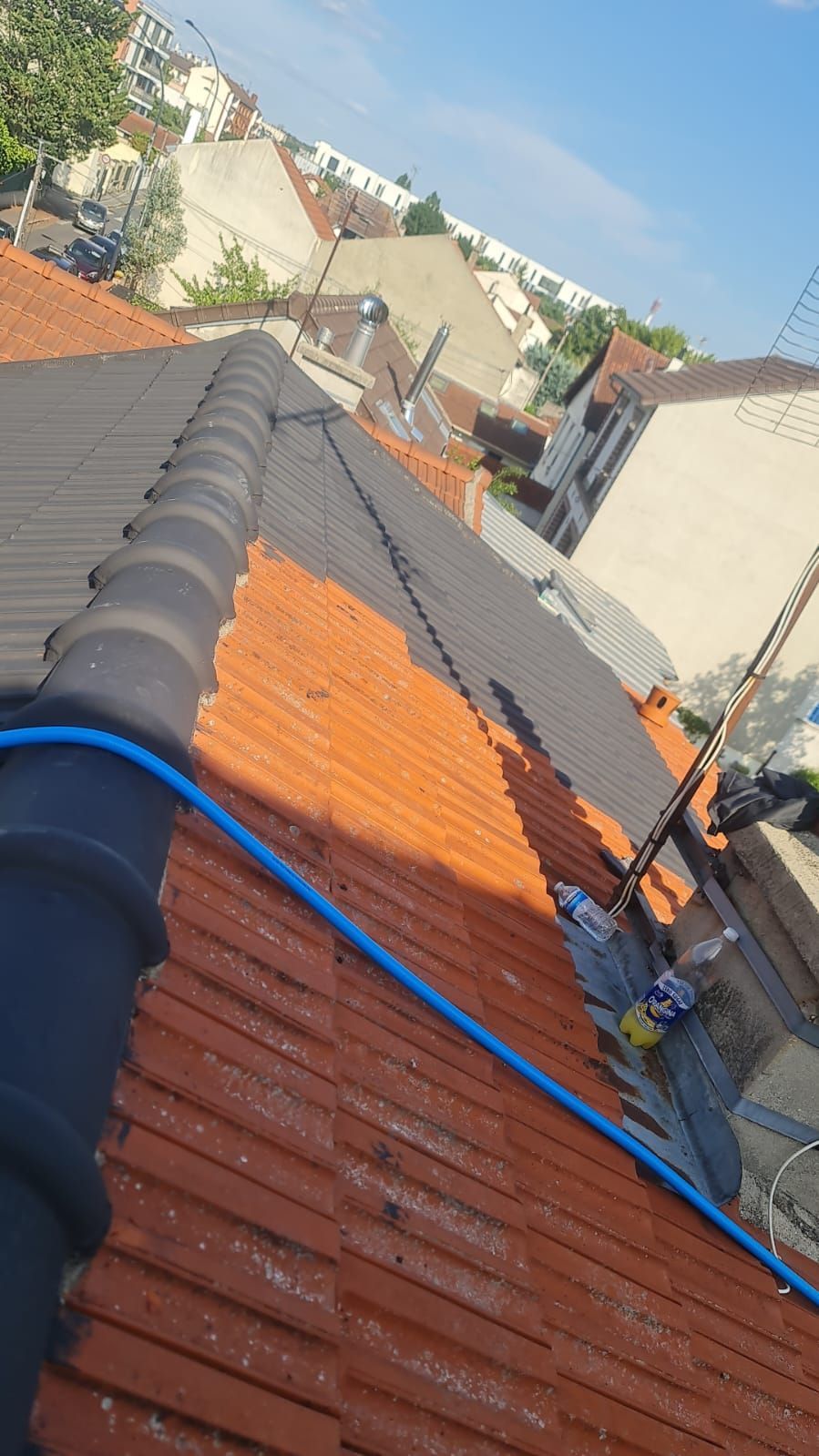 Vue depuis le toit avec des tuiles rouges, un câble bleu et les bâtiments environnants sous un ciel dégagé