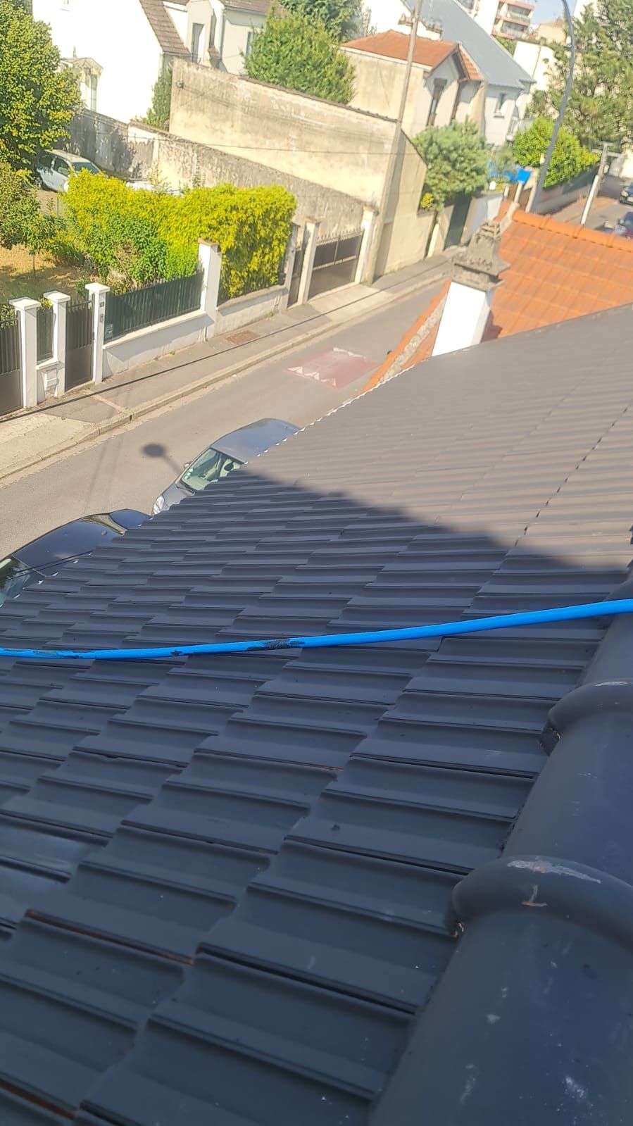 Vue depuis un toit en pente avec un câble bleu, donnant sur une rue résidentielle et des maisons en contrebas.