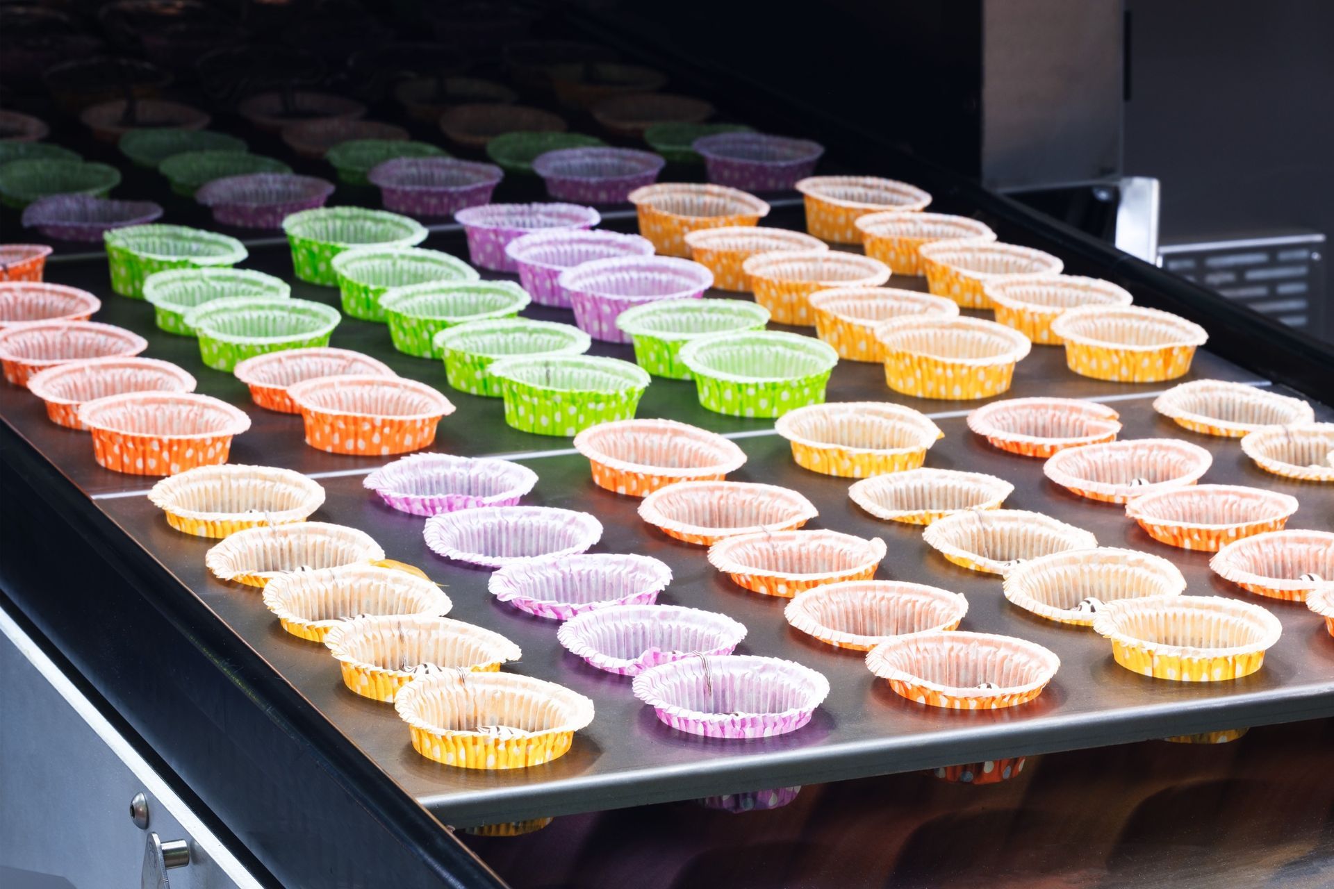 Una cinta transportadora llena de cupcakes de diferentes colores.
