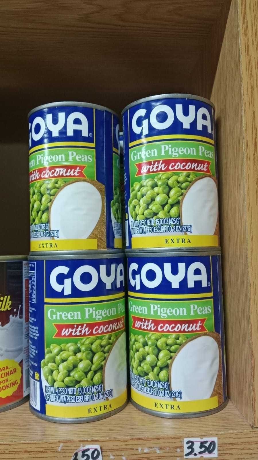 Latas de guisantes verdes Goya apiladas en un estante de madera con etiquetas de precio debajo.