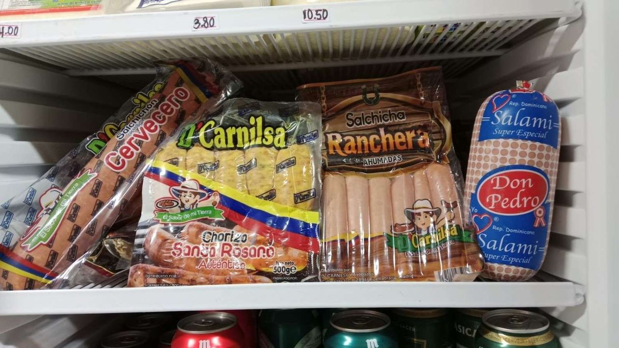 Surtido de salchichas y perritos calientes envasados ​​en un estante de supermercado, con etiquetas de precio encima.