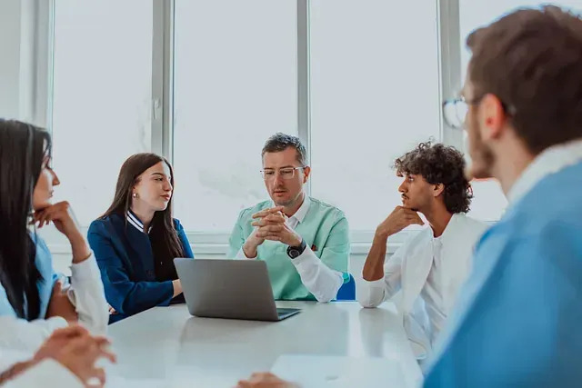 Un grupo de personas está sentado alrededor de una mesa con una computadora portátil.