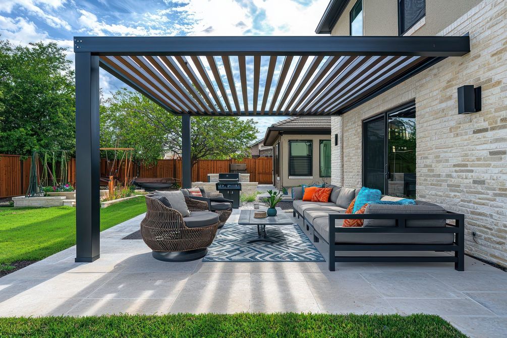 Patio de jardin moderne avec pergola, sièges en osier, canapé d'extérieur, tapis et façade de maison en pierre.