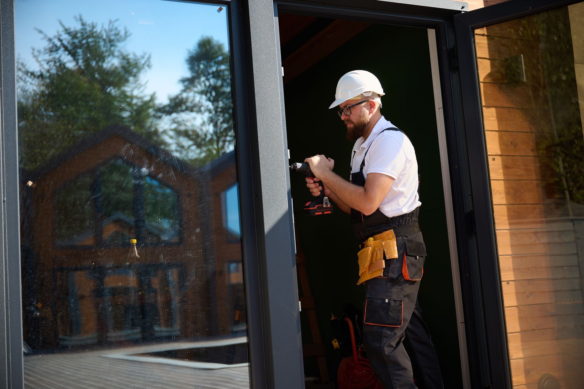 Ouvrier portant un casque de chantier installant une porte à l'entrée d'un bâtiment moderne.