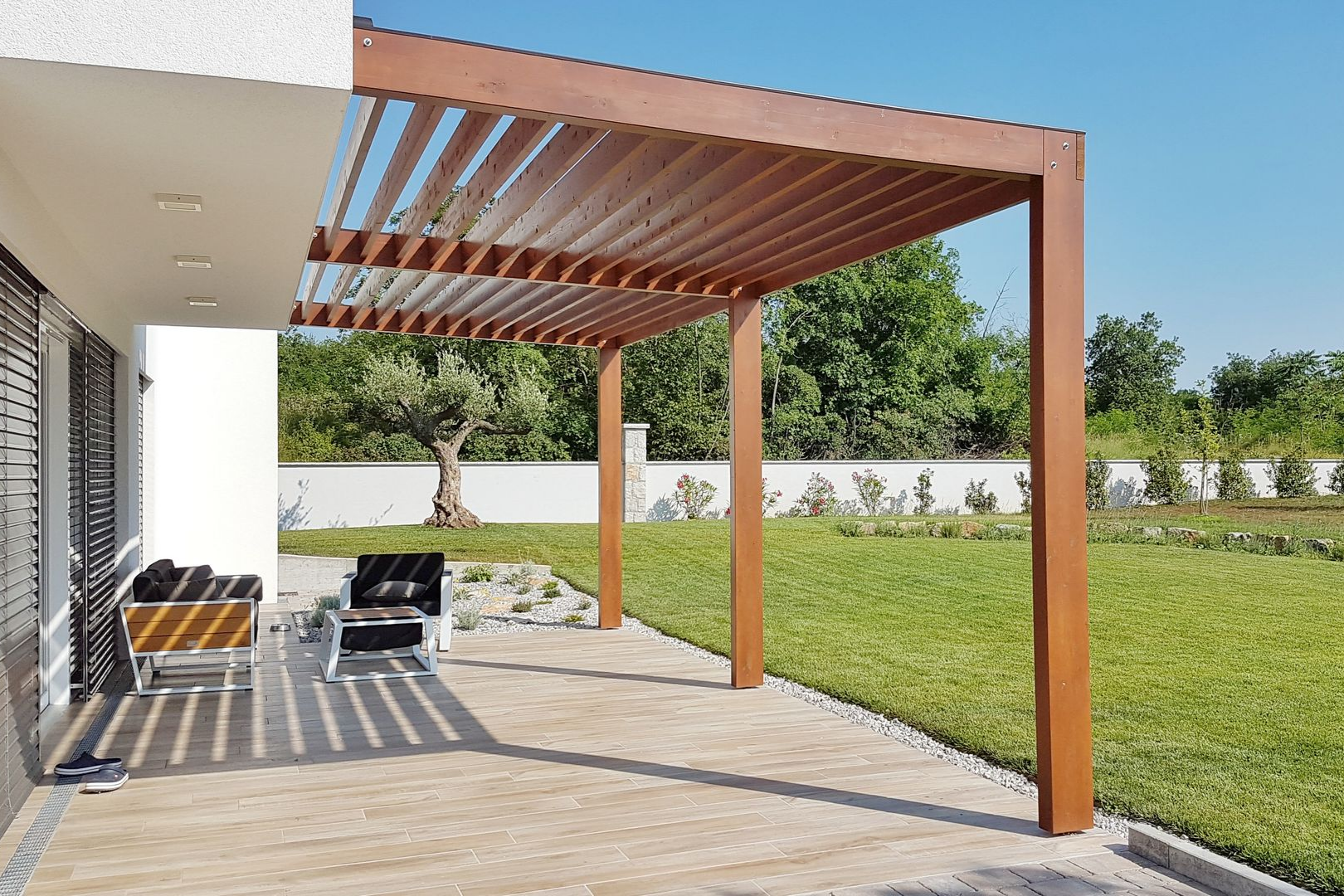 Patio moderne avec pergola en bois, sièges et pelouse ensoleillée à côté d'une maison.