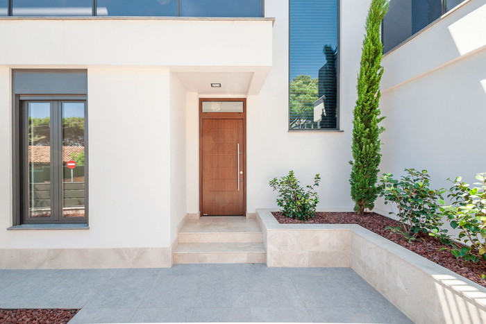 Entrée d'une maison blanche moderne avec porte d'entrée en bois, fenêtres et cour paysagée.