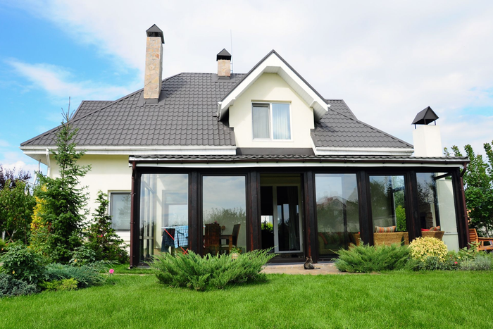 Maison blanche moderne avec véranda vitrée et pelouse verdoyante à l'avant.