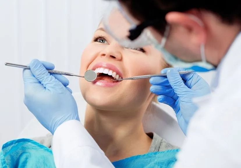 Un dentista, con guantes azules y gafas de seguridad, examina los dientes de un paciente utilizando un espejo dental.
