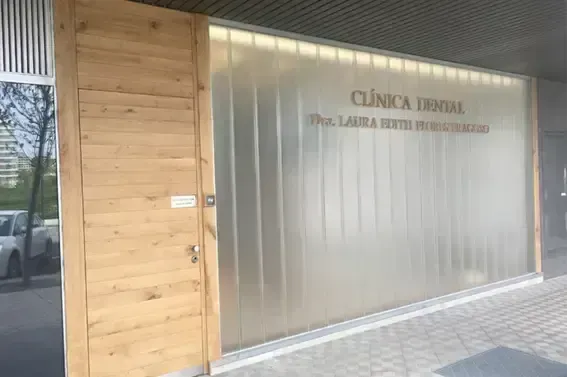 La entrada a una clínica dental con una puerta de madera junto a una pared de vidrio esmerilado con paneles verticales