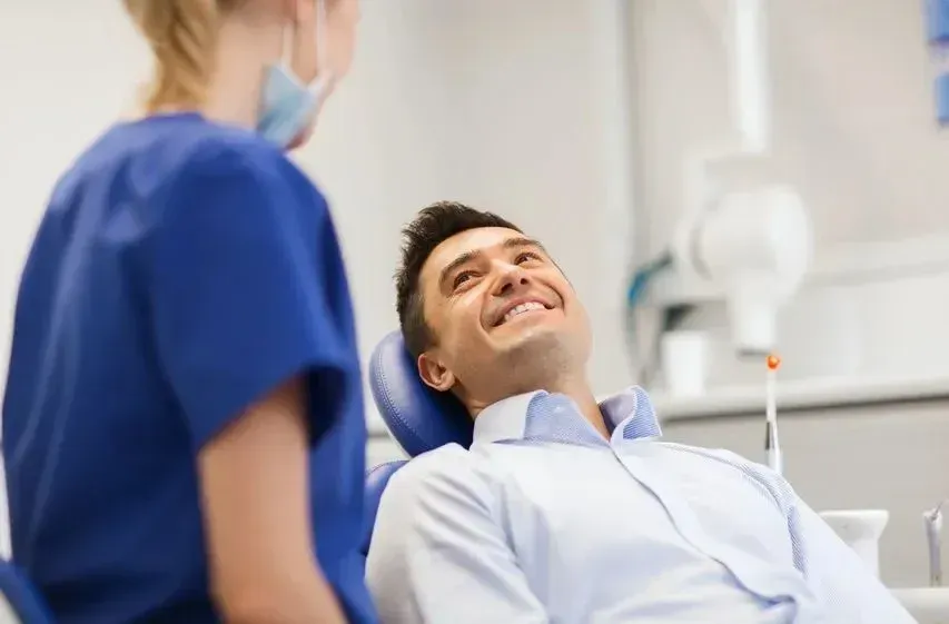 Una persona con una camisa azul claro sonríe sentada en un sillón dental
