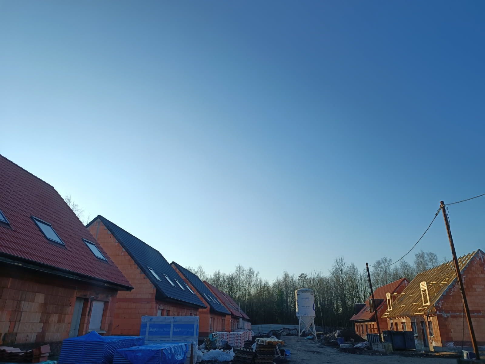 Rangée de maisons en briques aux toits de tuiles rouges sous un ciel bleu; matériaux de construction au premier plan.
