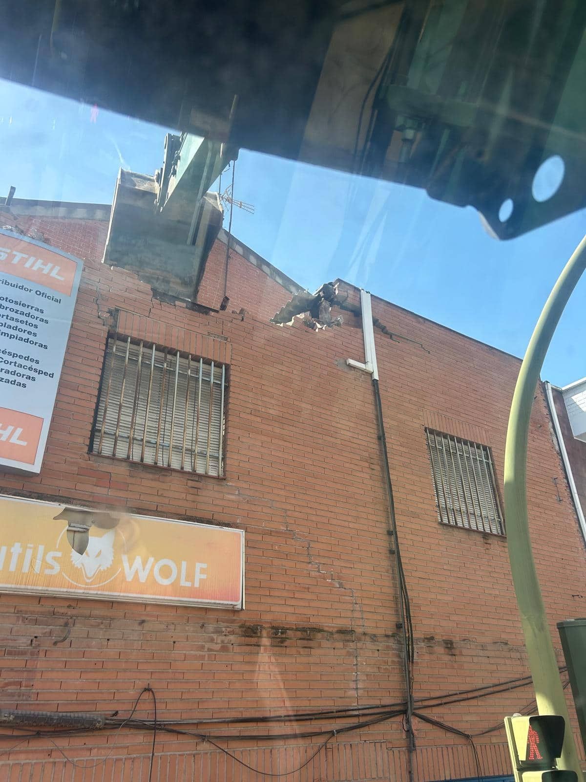 Edificio de ladrillo con el techo dañado. Señal de lobo bajo ventanas enrejadas. Cielo despejado.