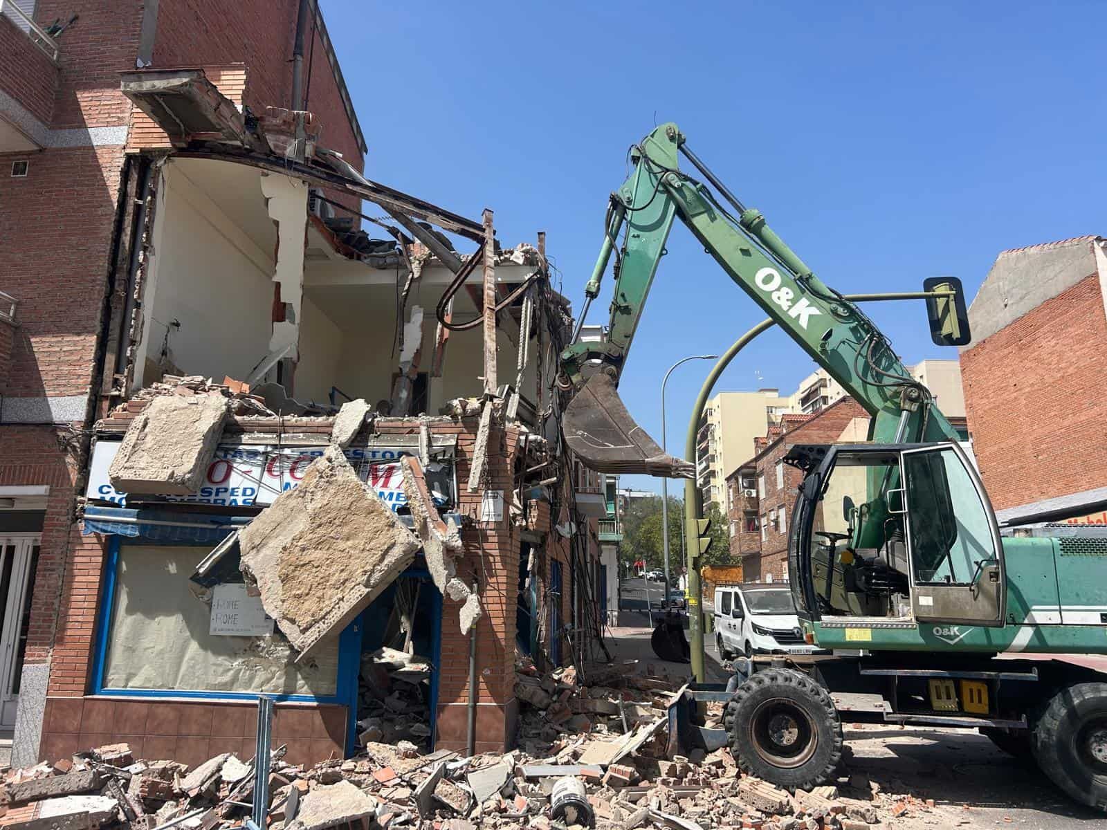 Excavadora demoliendo un edificio de ladrillos; cielo azul brillante, día soleado.