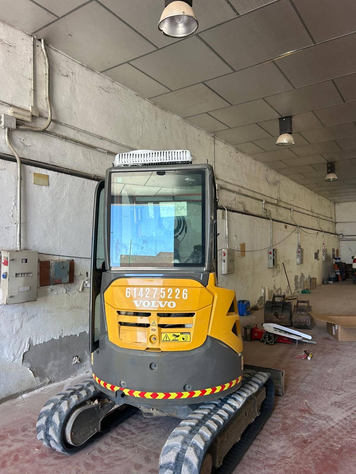 Excavadora Volvo amarilla dentro de un edificio con cableado expuesto y paredes de hormigón.