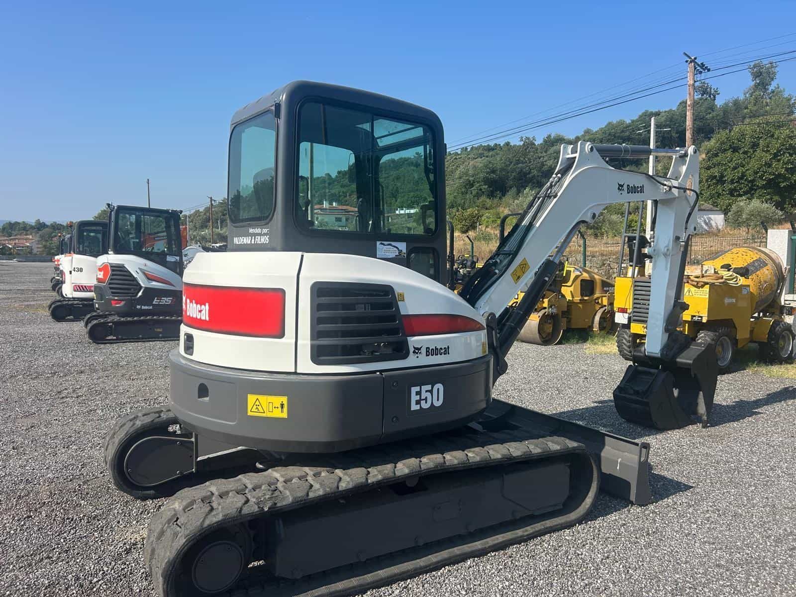 Excavadora compacta Bobcat E50 en lote de grava, blanca y gris con logotipo rojo.
