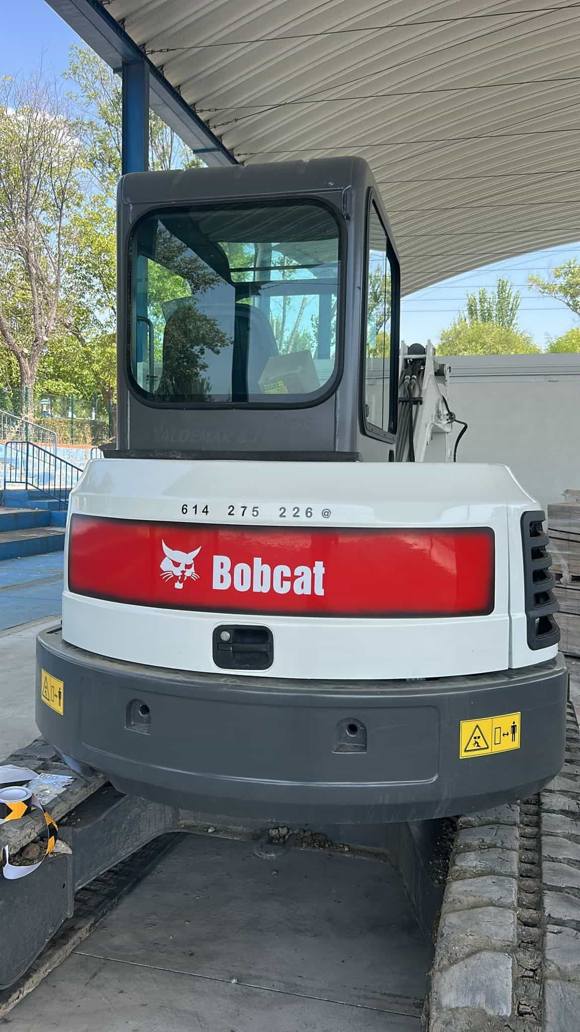 Excavadora Bobcat, carrocería blanca con logotipo rojo, en un entorno exterior soleado.