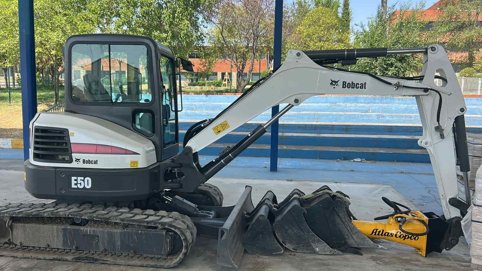 Excavadora Bobcat E50 con varios implementos estacionada sobre hormigón.