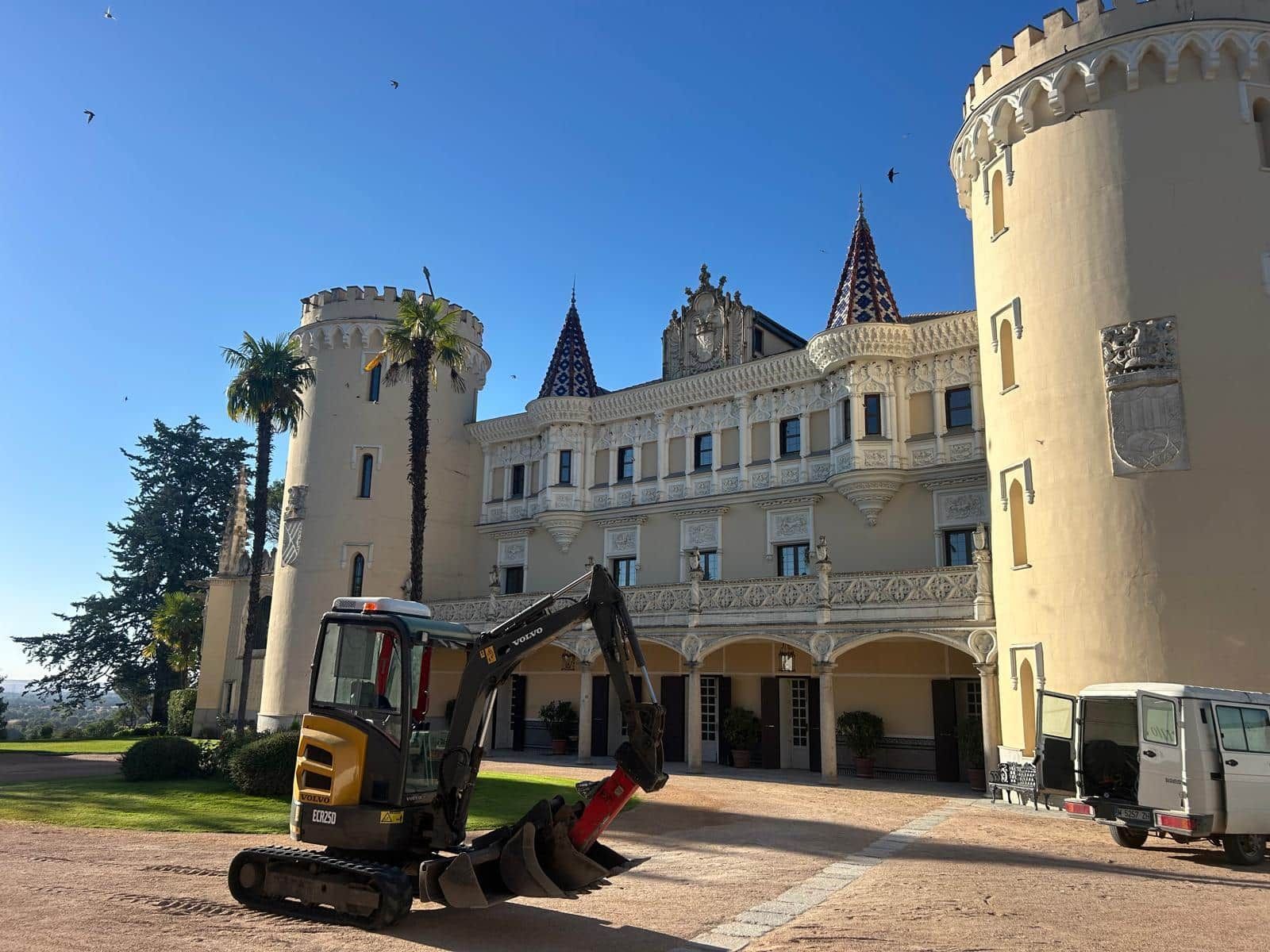 Una excavadora está delante de un castillo de color crema en un día soleado.