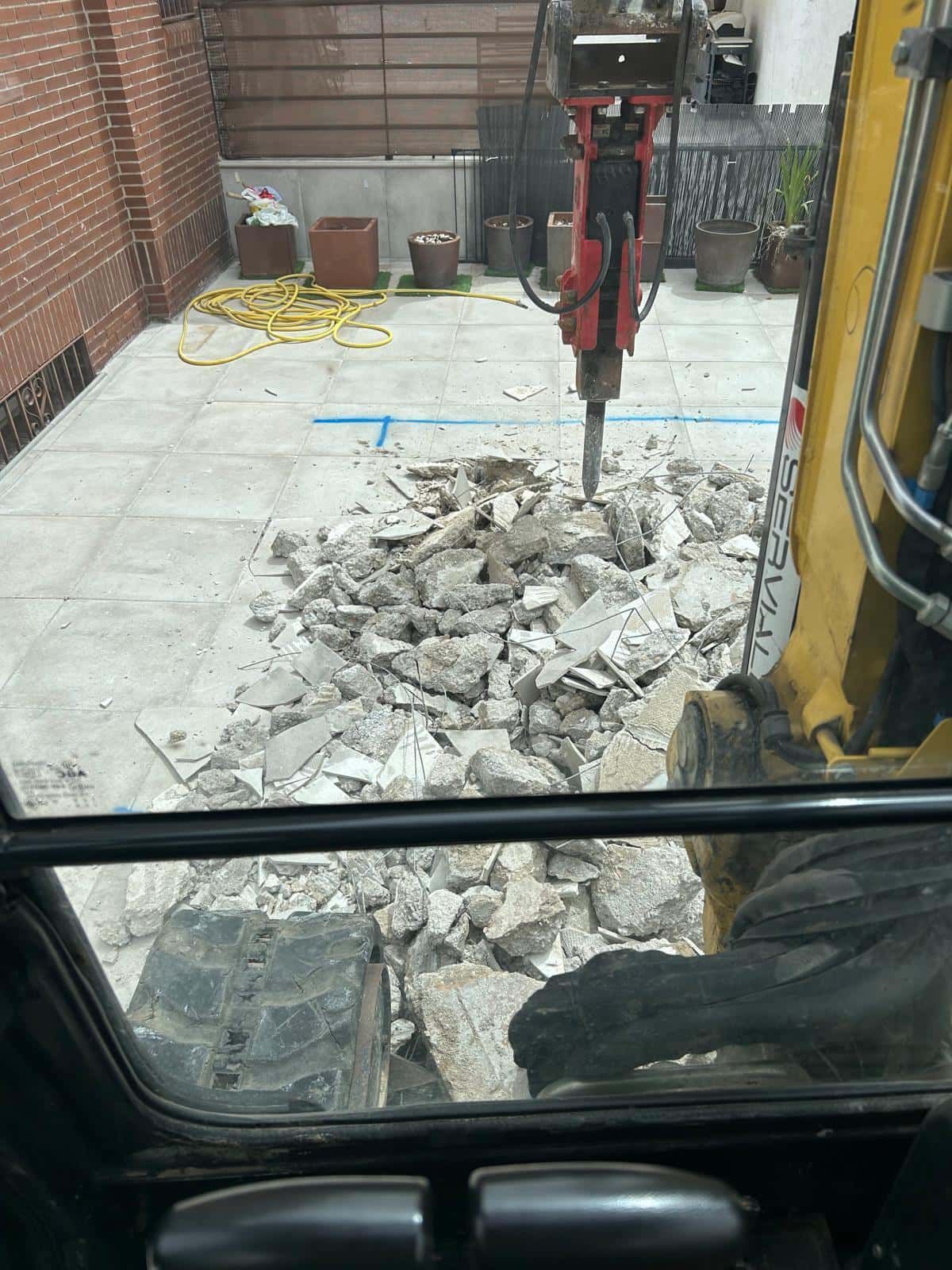 Demolición de un patio de hormigón con martillo hidráulico. La escena se observa desde el interior de la excavadora.