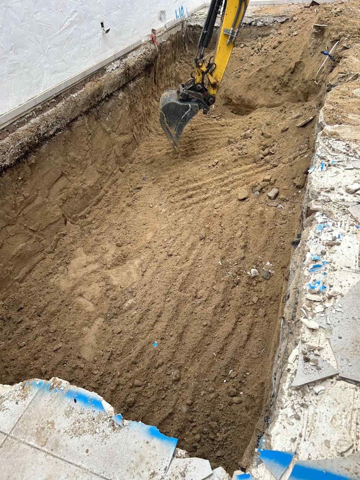 Excavadora en una zanja de una obra en construcción, excavando tierra cerca de una piscina.