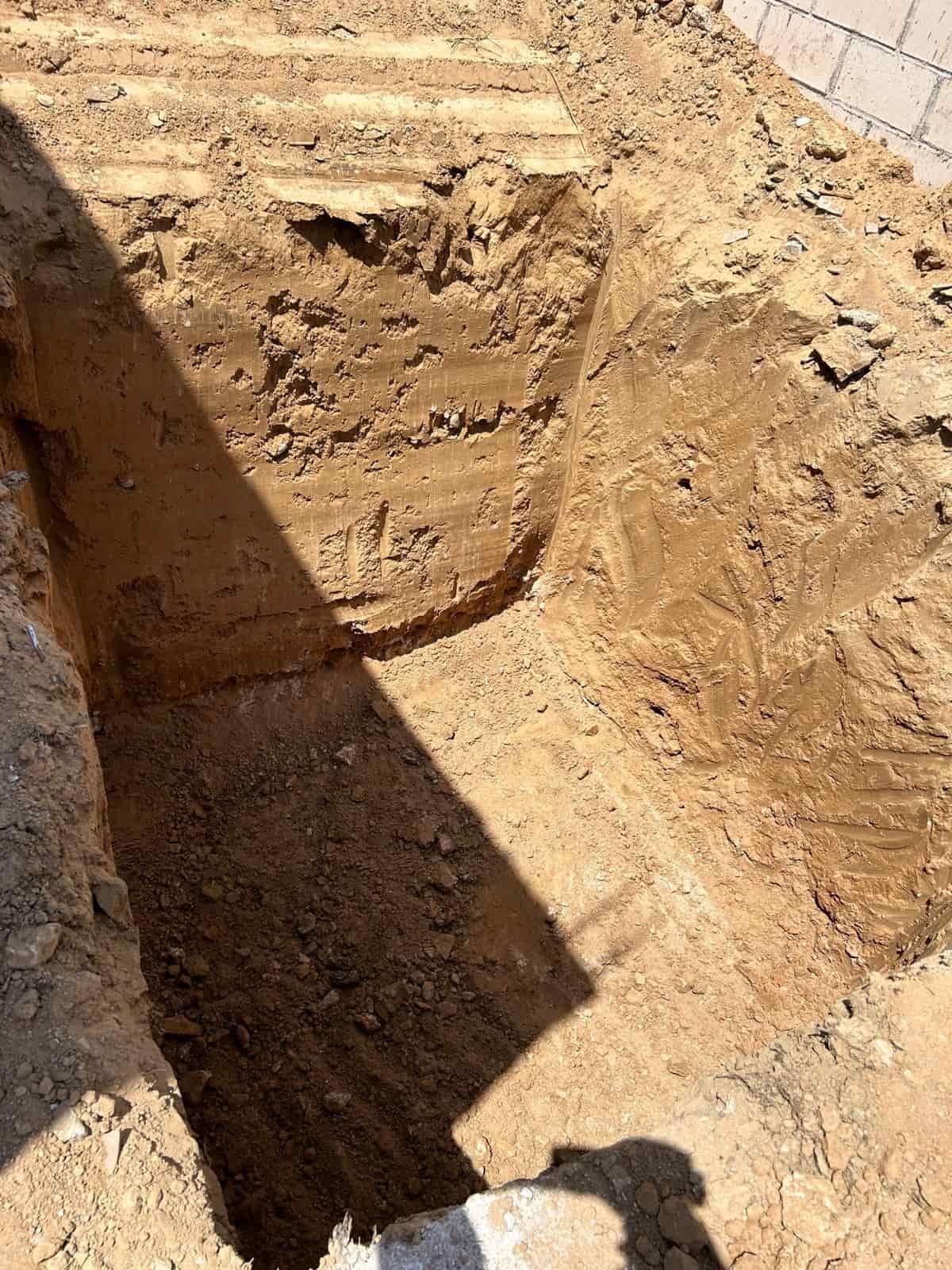 Una zanja de construcción profunda en suelo marrón con una sección curva, al aire libre bajo la luz del sol.