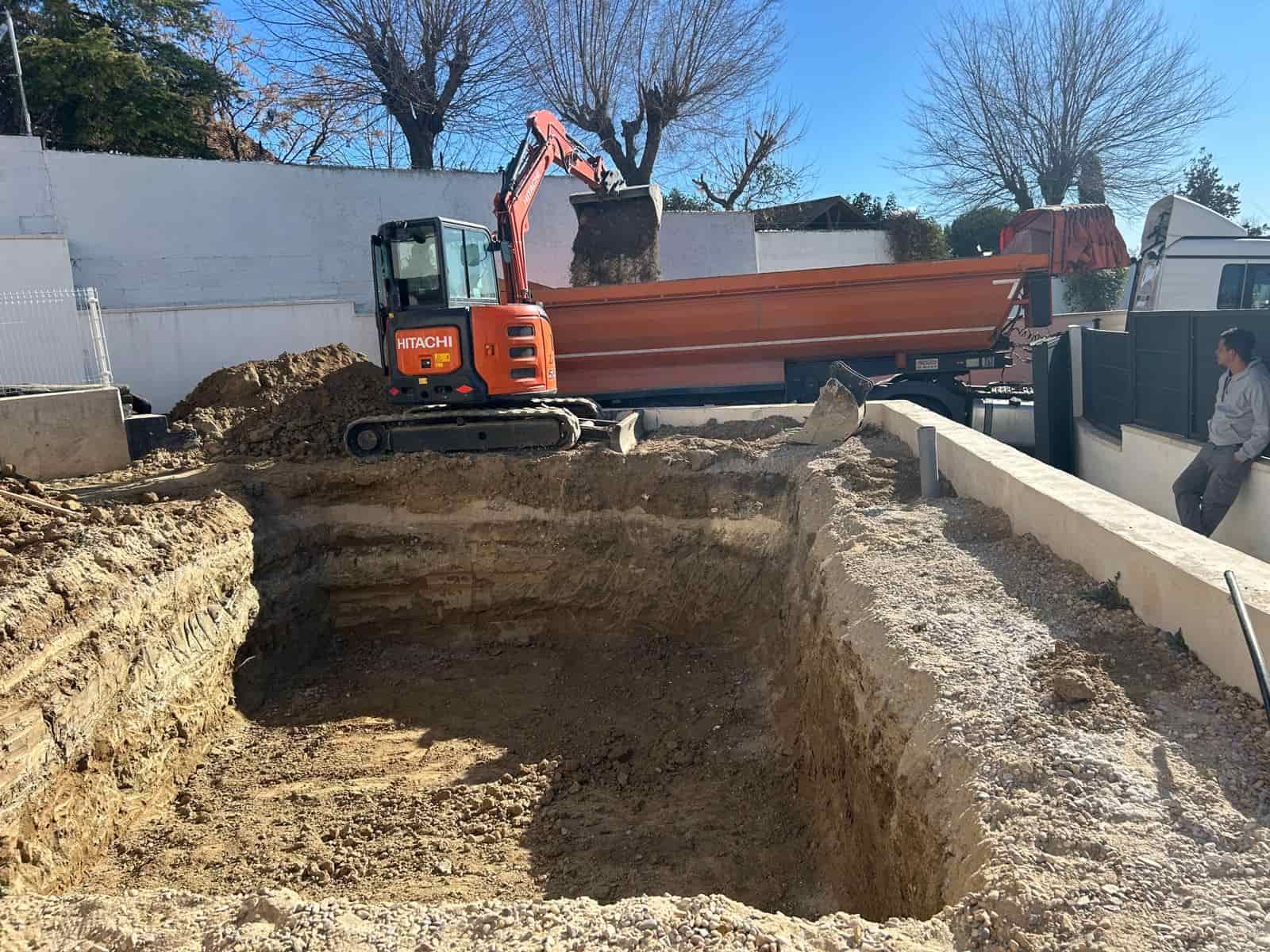 Miniexcavadora cargando un camión volquete con tierra de un gran pozo de excavación al aire libre en un día soleado.