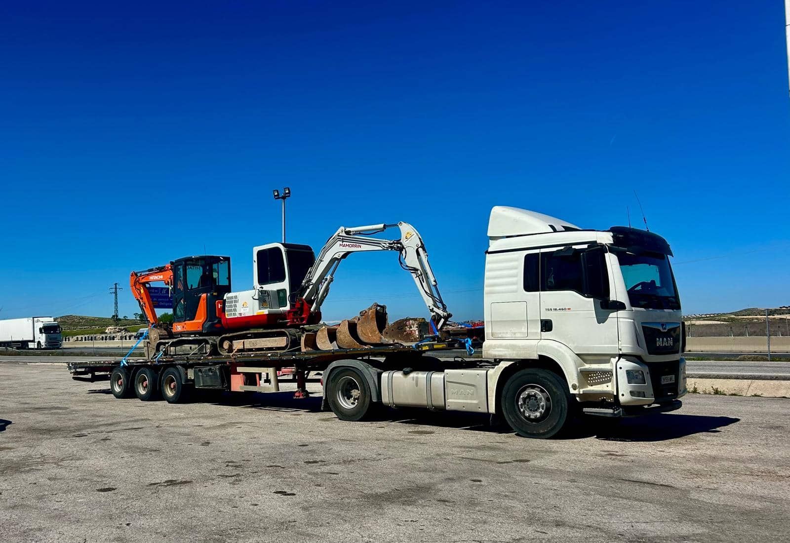 Camión con excavadora sobre remolque de plataforma, bajo un cielo azul claro.