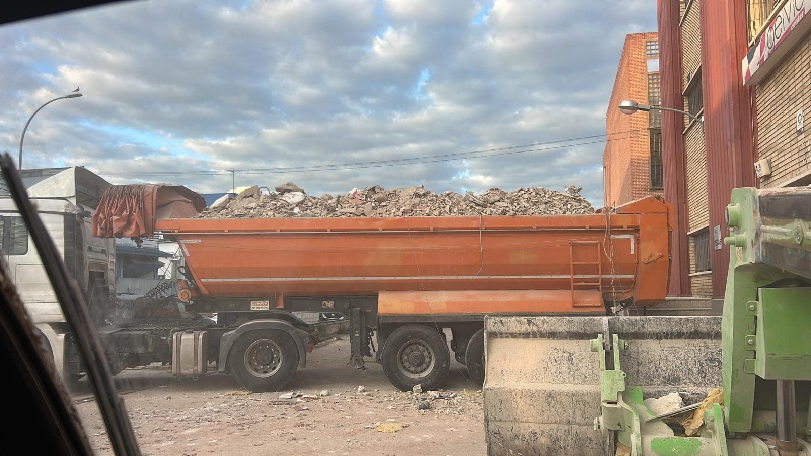 Camión volquete naranja lleno de escombros de construcción estacionado al lado de un edificio de ladrillos.