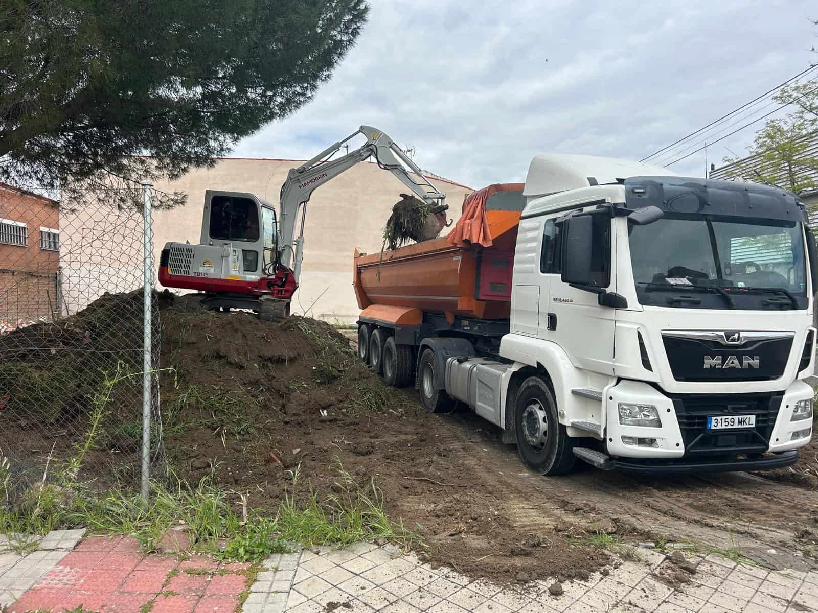 Una excavadora carga tierra en un camión volquete naranja en un sitio de construcción.
