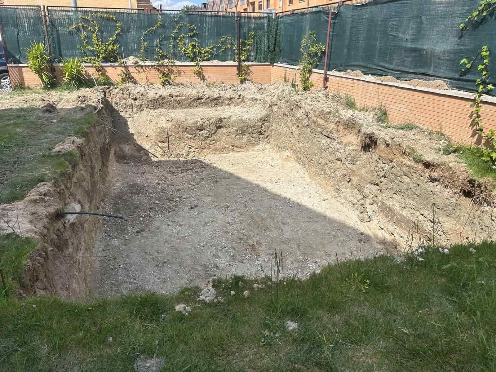 Pozo trasero excavado de forma rectangular, rodeado de césped y pared de ladrillo.