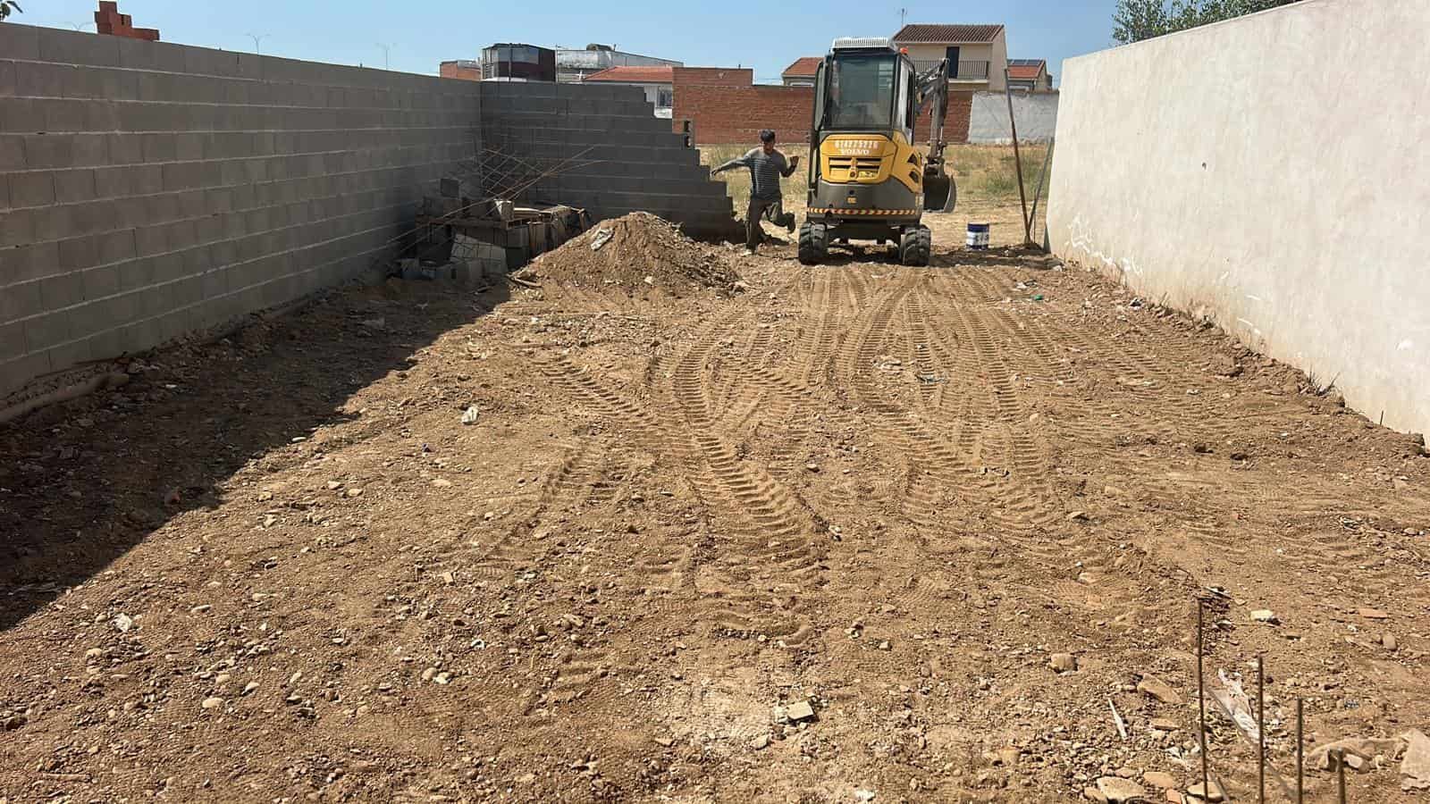 Una excavadora moviendo tierra en un sitio de construcción rodeado de muros de hormigón.