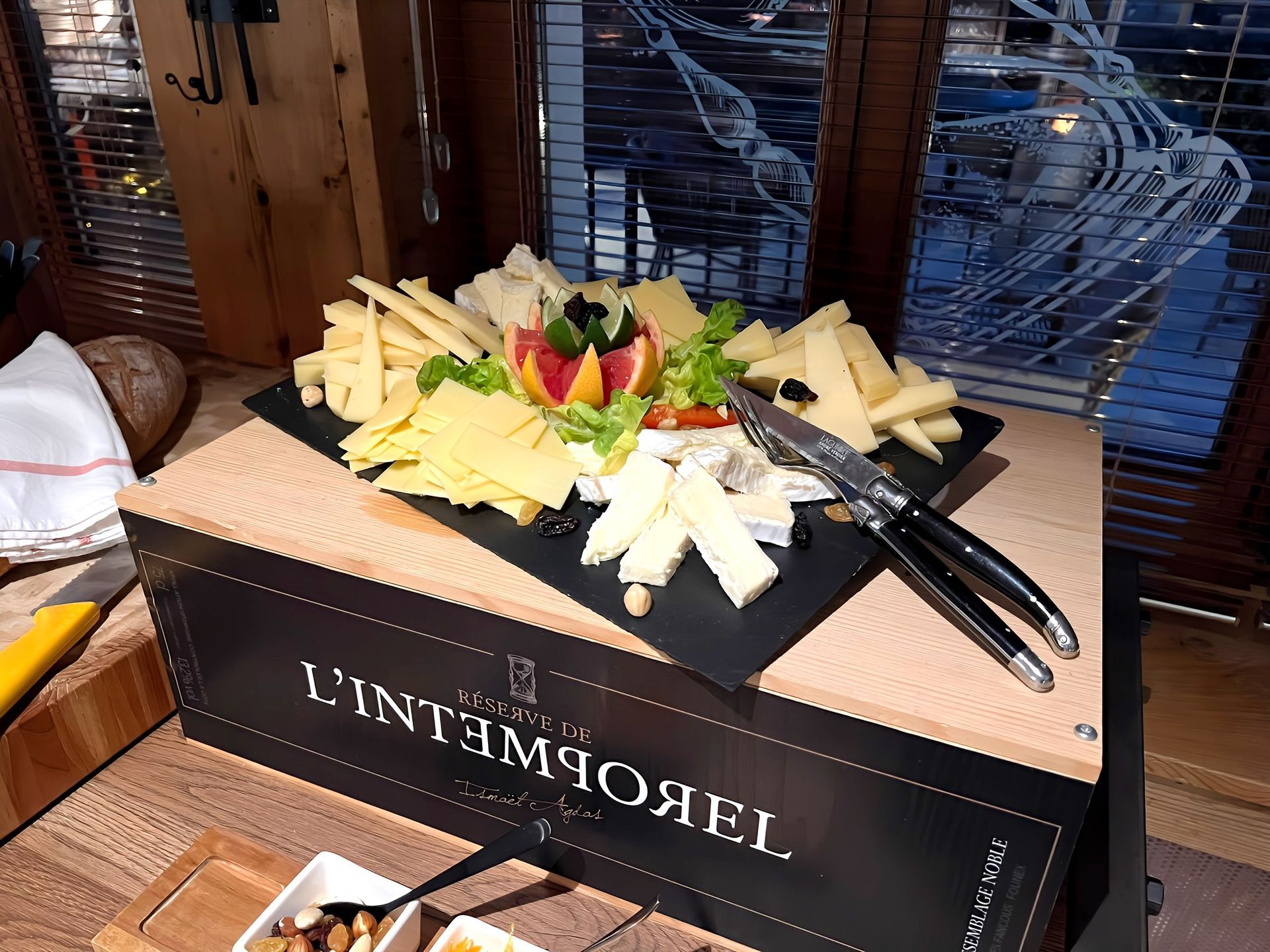 Plateau de fromages avec assortiment de quartiers, raisins et pinces sur un présentoir noir à une table de buffet