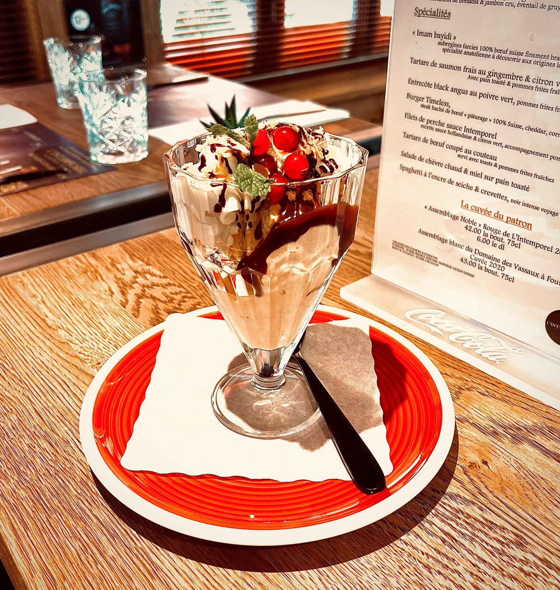 Parfait au chocolat servi dans un verre sur une assiette à bord rouge, garni de fraises, sur une table de café