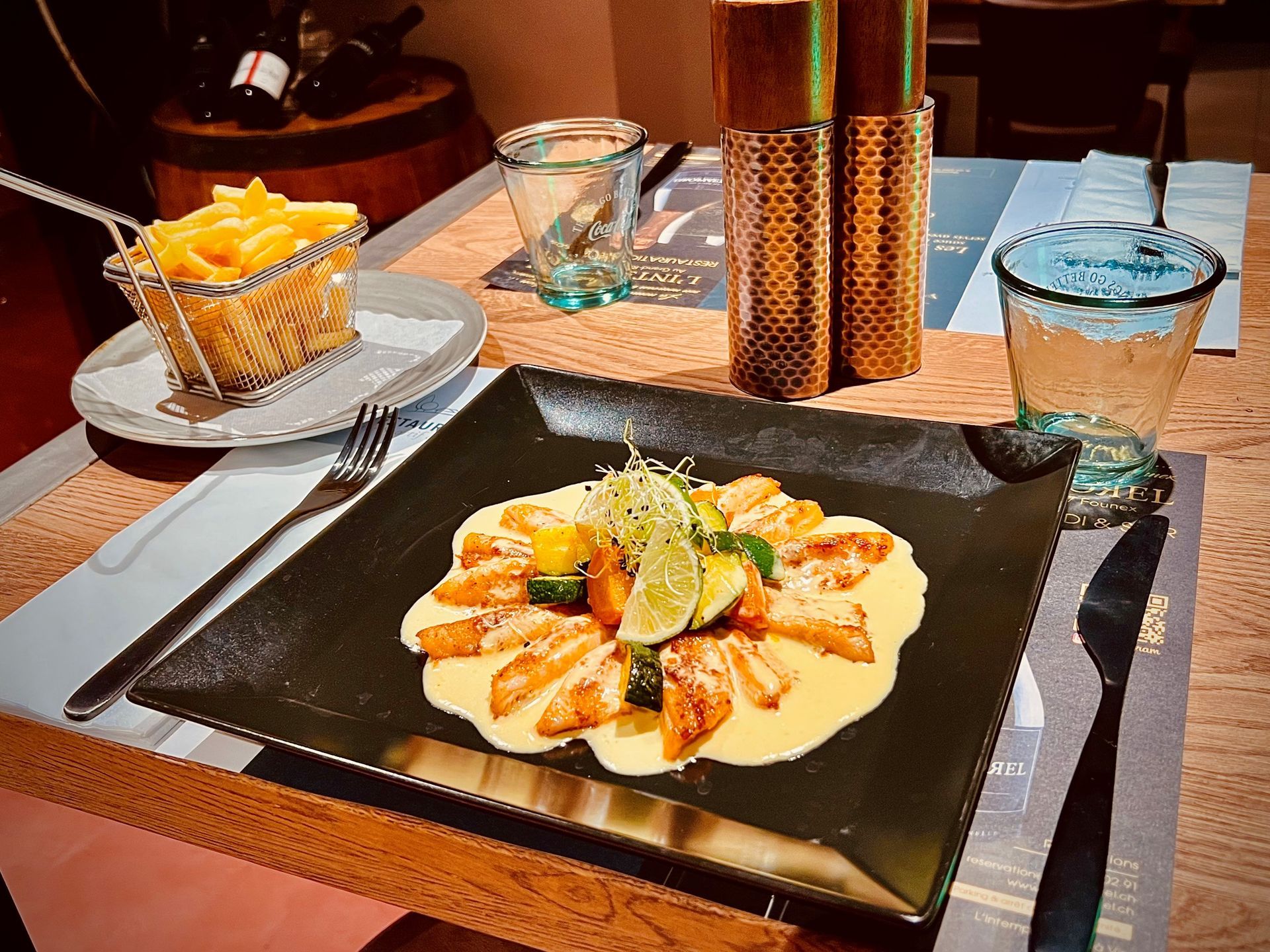 Plat de pâtes garni de citron vert, présenté sur une table de café, à côté d'un verre de jus d'orange et d'une boisson bleue.